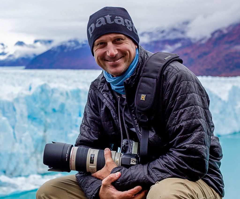 Travel photographer sitting on the edge of Perito Moreno Glacier in Patagonia, Argentina, surrounded by blue ice formations in winter