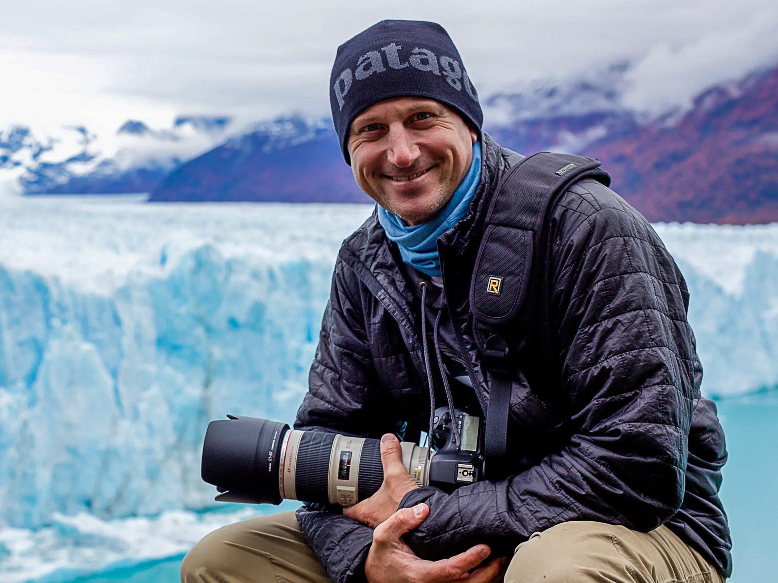 Travel photographer sitting on the edge of Perito Moreno Glacier in Patagonia, Argentina, surrounded by blue ice formations in winter